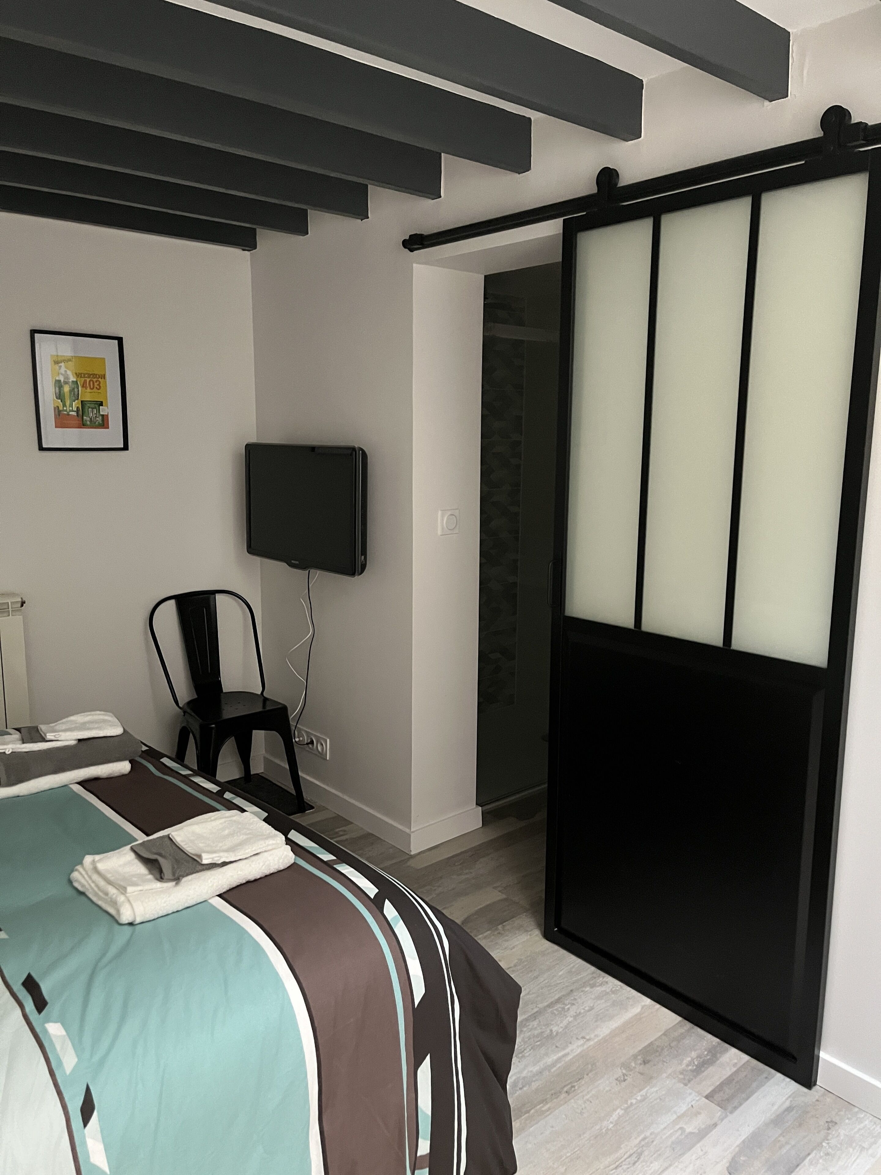 Ein modernes Hotelzimmer mit Bett, Sessel, Fernseher und einer Schiebetür.