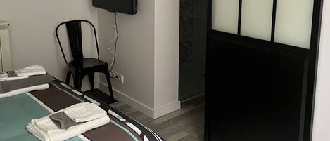 Ein modernes Hotelzimmer mit Bett, Sessel, Fernseher und einer Schiebetür.