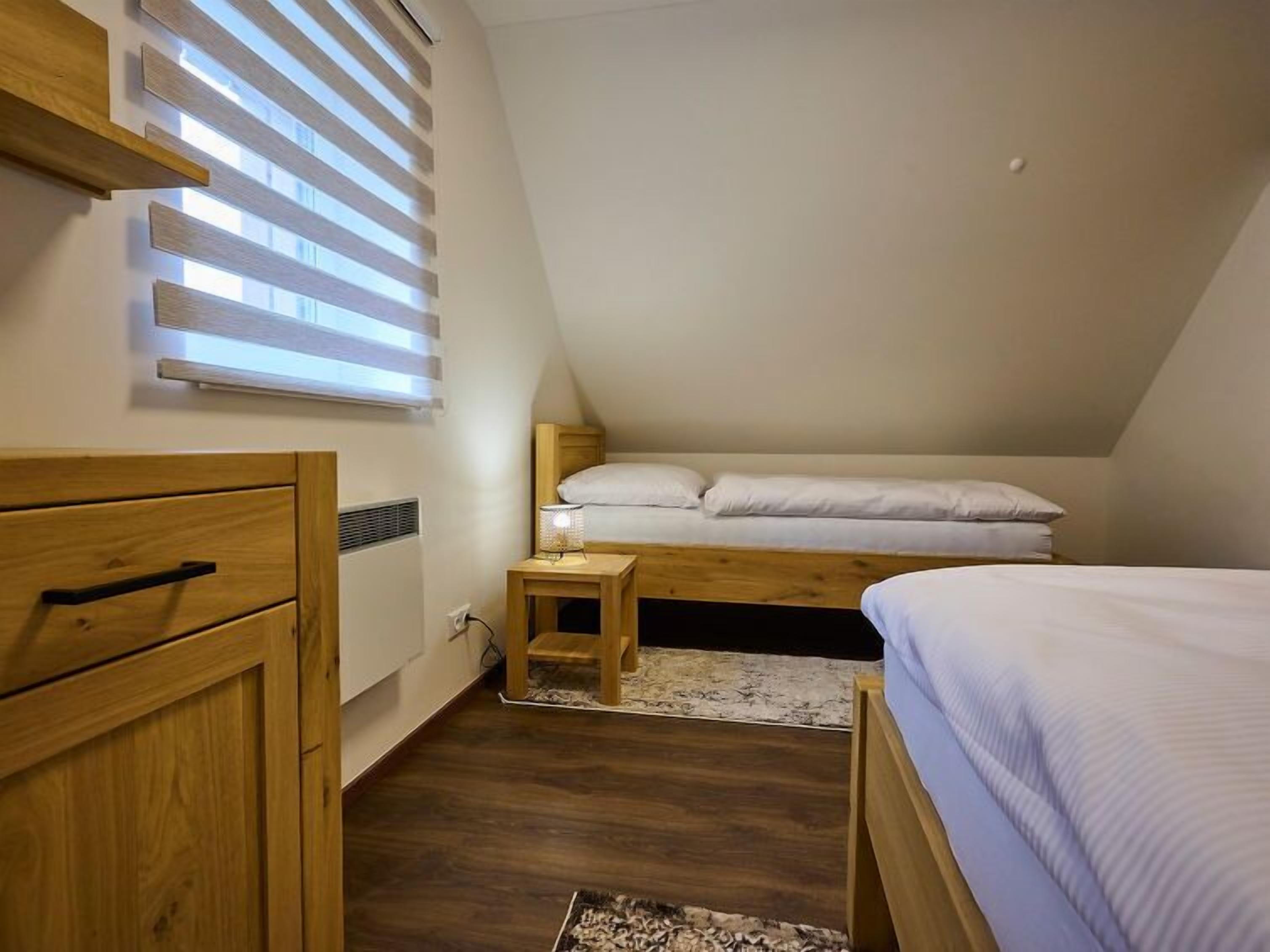 A bedroom with a sloped ceiling, wooden furniture, a bed with white bedding, and a small bedside table with a lamp.