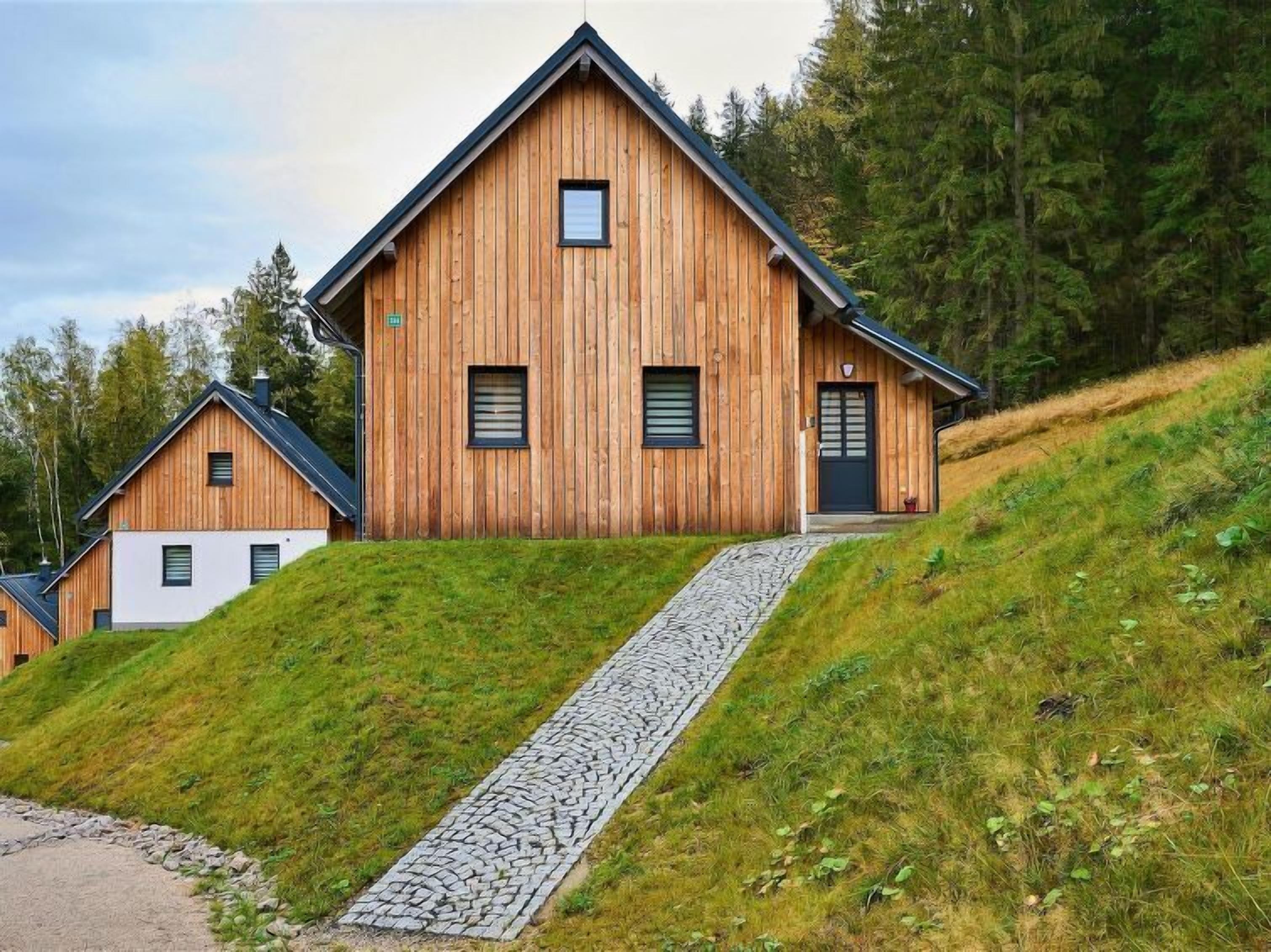 Une cabane en bois avec un toit en pente, un chemin de pierres menant à l’entrée et une colline verdoyante.
