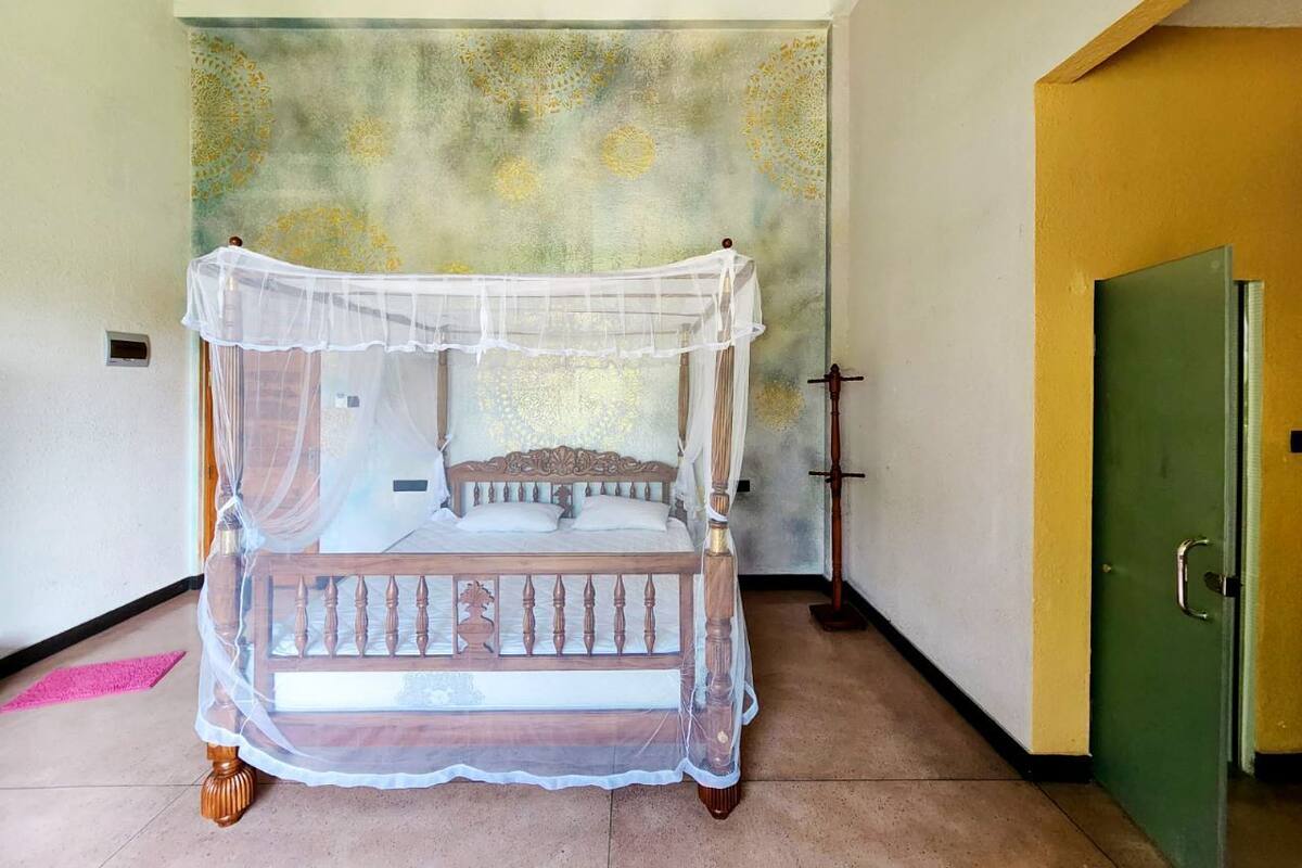 Une chambre avec un lit à baldaquin, une porte verte et un mur orné de motifs.