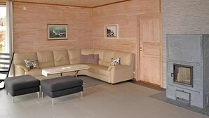 Ein modernes Wohnzimmer mit einem beigefarbenen Ecksofa, zwei schwarzen Hocker, einem kleinen weißen Couchtisch und einem Kamin.