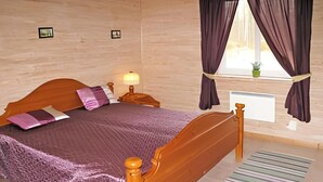 Ein Schlafzimmer mit einem hölzernen Bett, einem Nachttisch mit Lampe, einem Fenster mit Vorhängen und einer Heizung.