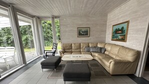 Ein modernes Wohnzimmer mit einem beigen Ledersofa, einem schwarzen Hocker und einem Couchtisch. An der Wand hängt ein Gemälde und es gibt ein Fenster mit Vorhängen.