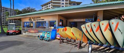 A building with a sign for 'Beach Activities Water Sports Center' and a row of surfboards.