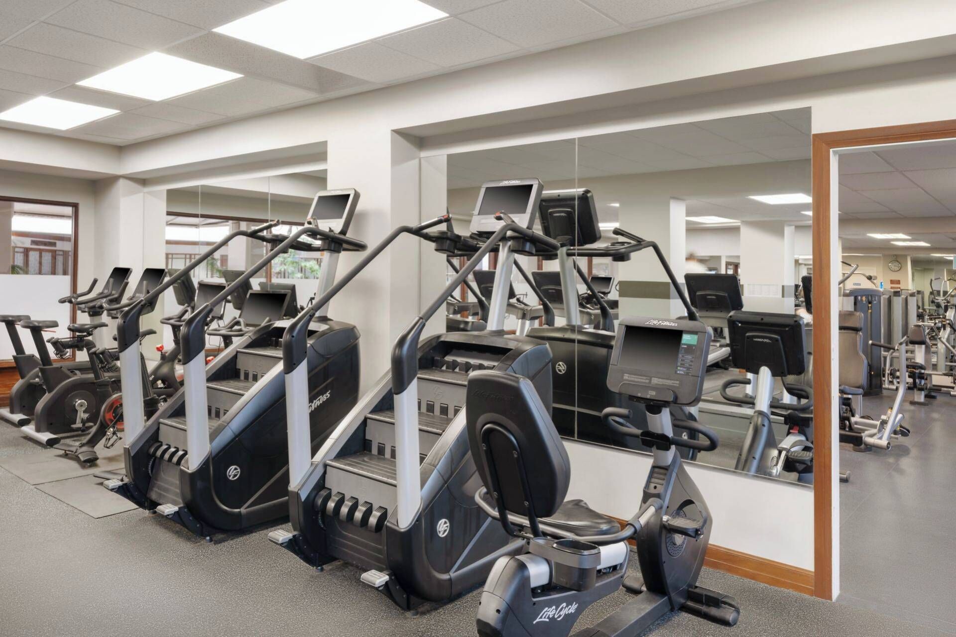 A gym with multiple cardio machines, mirrors, and exercise equipment.