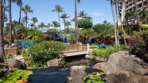 Ein Resort mit Pool, Palmen, einem Wasserfall und einer Brücke.