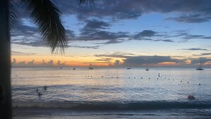 Une plage avec des bateaux sur l’eau et un coucher de soleil en arrière-plan.