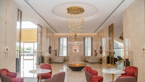 A spacious lobby with modern red and grey chairs, a central fire feature, and a chandelier. - LC International Hotel (Yangon)