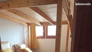 Ein kleines, gemütliches Zimmer mit einem Holzbett, einem Fenster mit Vorhängen und einem grünen Teppich.