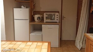 Eine kompakte Küchenzeile mit Kühlschrank, Mikrowelle und Geschirrspüler. Ein Willkommensschild hängt an der Tür, und darüber befinden sich Regale.
