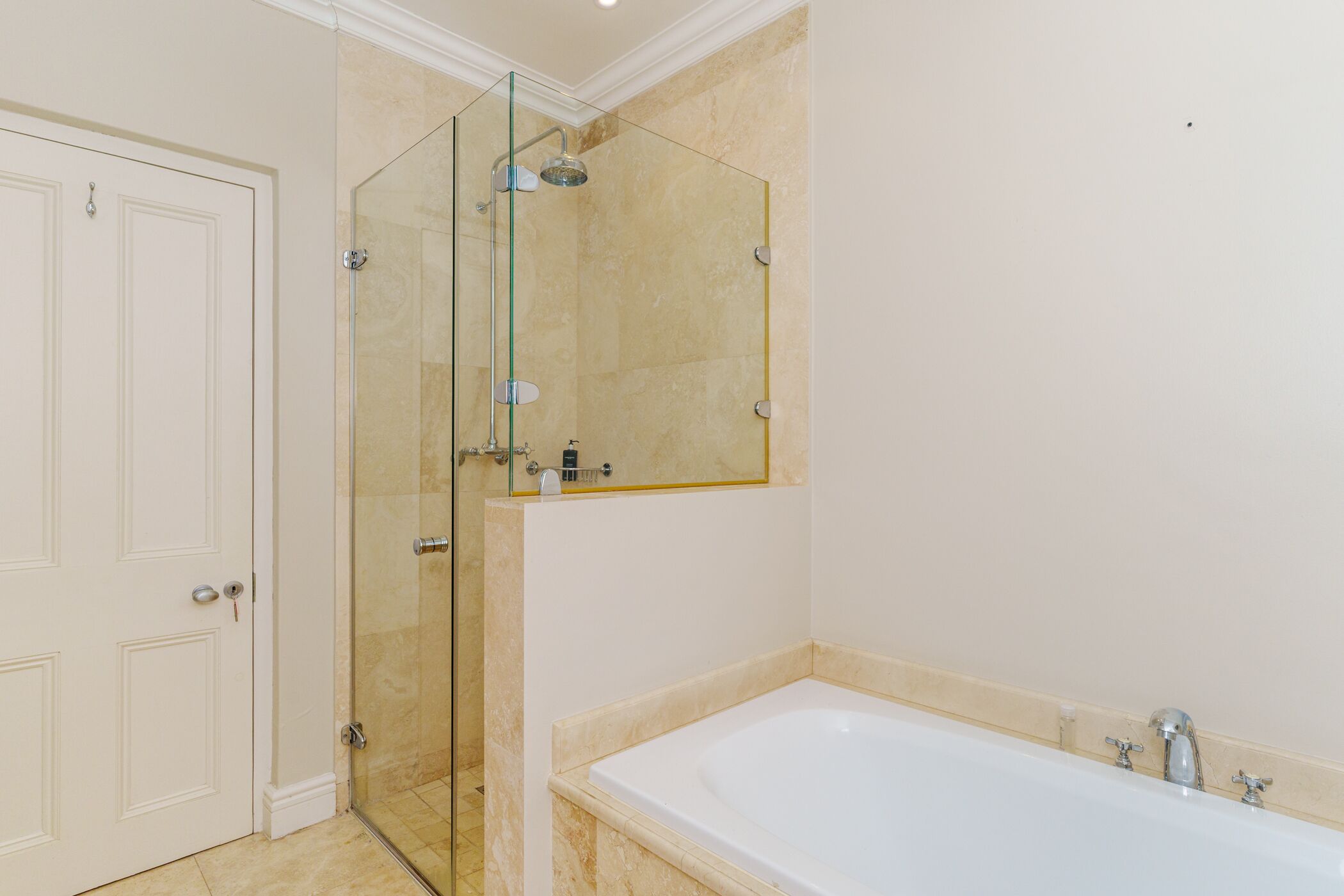 A bathroom with a glass-enclosed shower, a white bathtub, and a door.