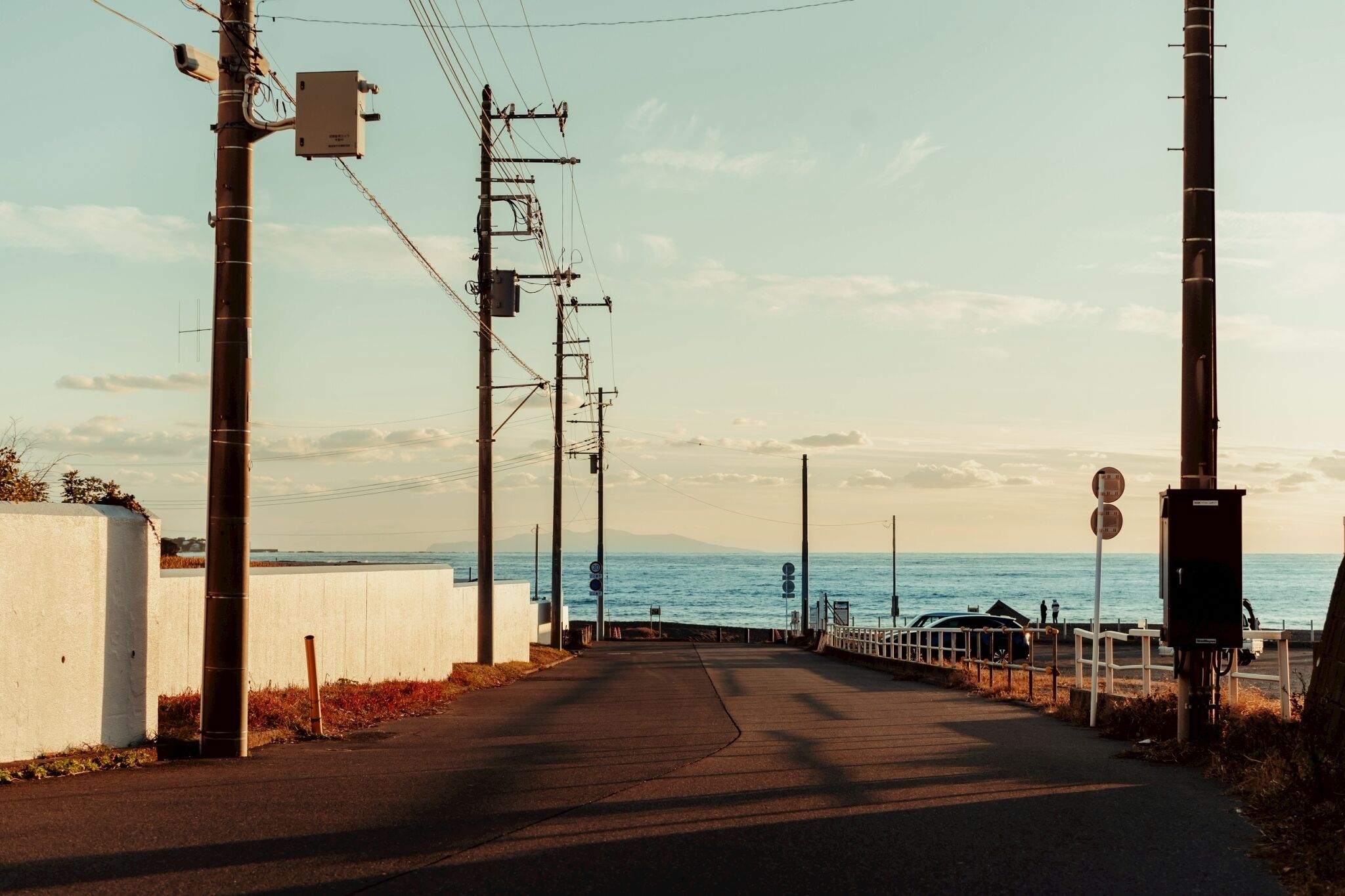 Une route côtière bordée de poteaux électriques, un mur blanc et une vue sur la mer.
