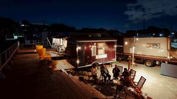 A small, compact RV-style accommodation with a wooden deck and outdoor seating area.