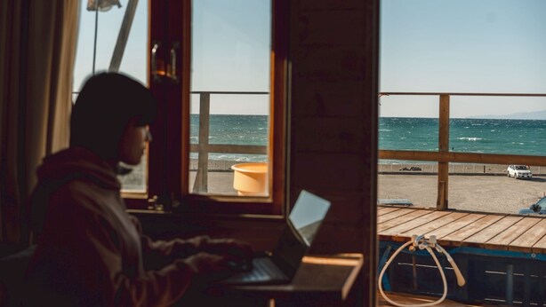 A person using a laptop on a balcony with a view of the sea and a parked car. - ZEKKEI SEASIDE NAHAMA (Yokosuka)
