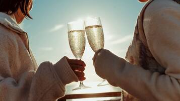 Two people toasting with champagne glasses, a clear sky, and a sunset in the background.