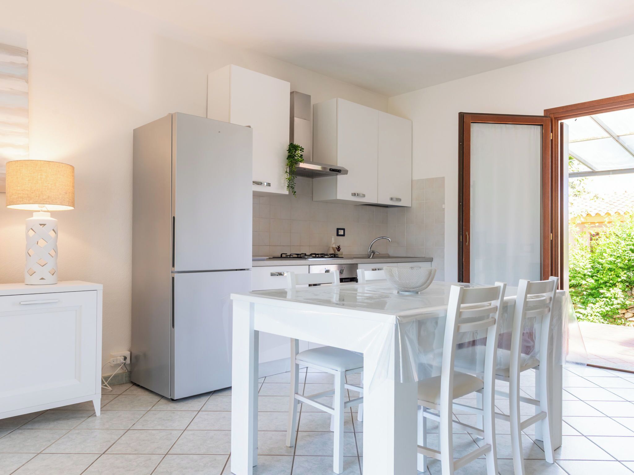 Una cocina moderna con armarios blancos, estufa integrada y comedor con mesa y sillas de vidrio.