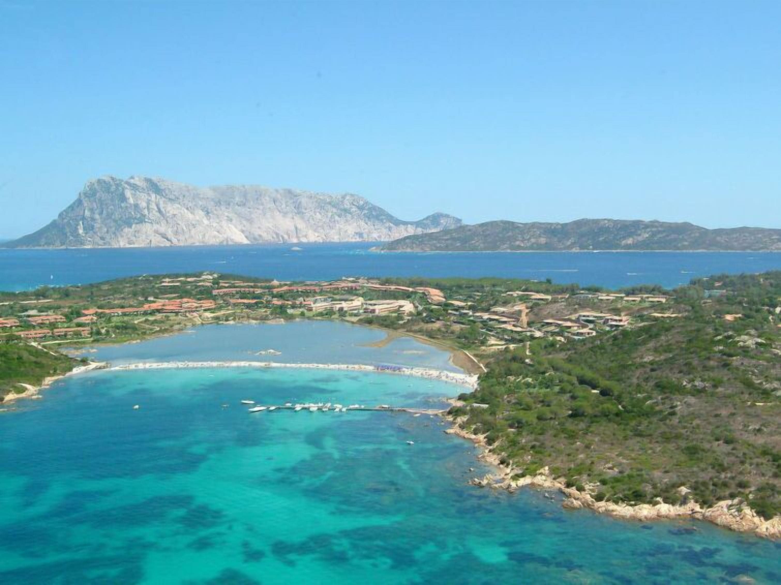 A coastal resort with clear turquoise waters, a rocky mountain backdrop, and a mix of residential and natural areas.