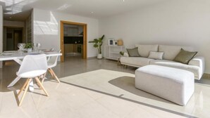 A modern living room with a white sofa, a dining table with chairs, and a kitchen visible through an open door. - Lizarran by Interhome (Figueres)