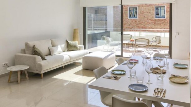A modern living room with a white sofa, a dining table set for four, and a balcony with outdoor seating. - Lizarran by Interhome (Figueres)