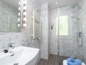 Bathroom features a large bathtub, glass-enclosed shower with handheld showerhead, and wall-mounted faucet.