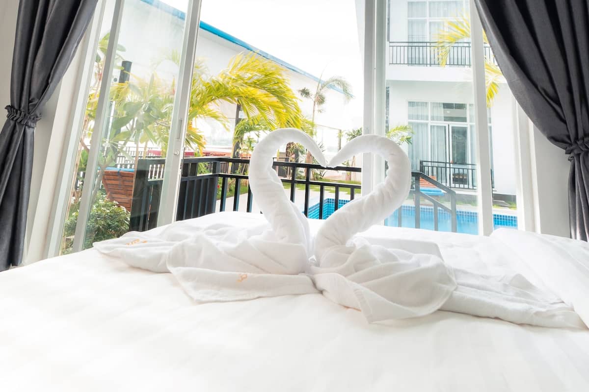 A hotel room with a bed, a large window, and a view of a building and palm trees outside.