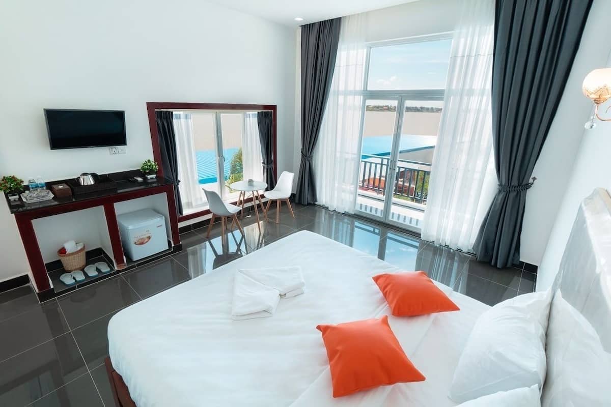 A hotel room with a large bed, a TV, a desk, a chair, and a balcony with a view.
