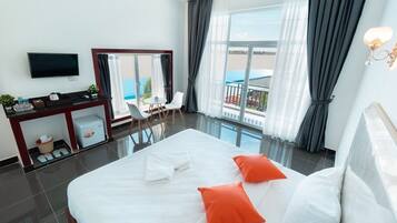 A hotel room with a large bed, a TV, a desk, a chair, and a balcony with a view.