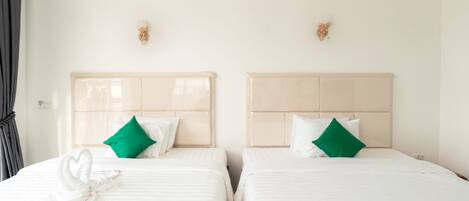 Dos camas individuales con ropa de cama blanca y almohadas verdes, una toalla blanca y un aplique en la pared.