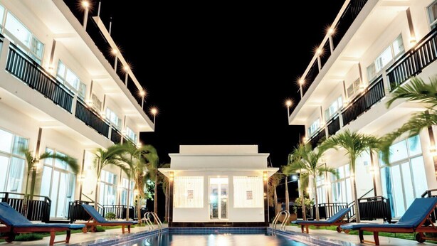 A swimming pool with lounge chairs and palm trees, surrounded by a modern building with balconies and large windows. - Koh Dach View Boutique (Phnom Penh)