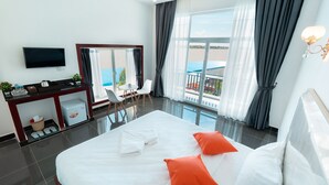 A hotel room with a large bed, a desk with a TV, a chair, and a view of the pool. - Koh Dach View Boutique (Phnom Penh)