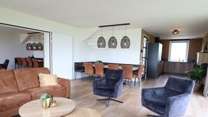 Una sala de estar moderna con un sofá, dos sillones, una mesa de centro y un comedor con sillas y una mesa.
