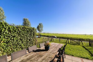 A wooden table with chairs and a potted plant, set against a backdrop of a green field and a clear blue sky. - Stylish Frisian Villa with Garden (Leons)