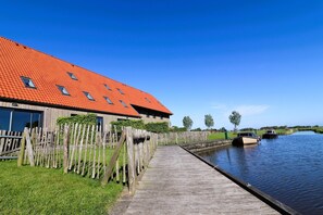 En træbro fører ud til en kanal med et hus, rødt tag og et hegn.