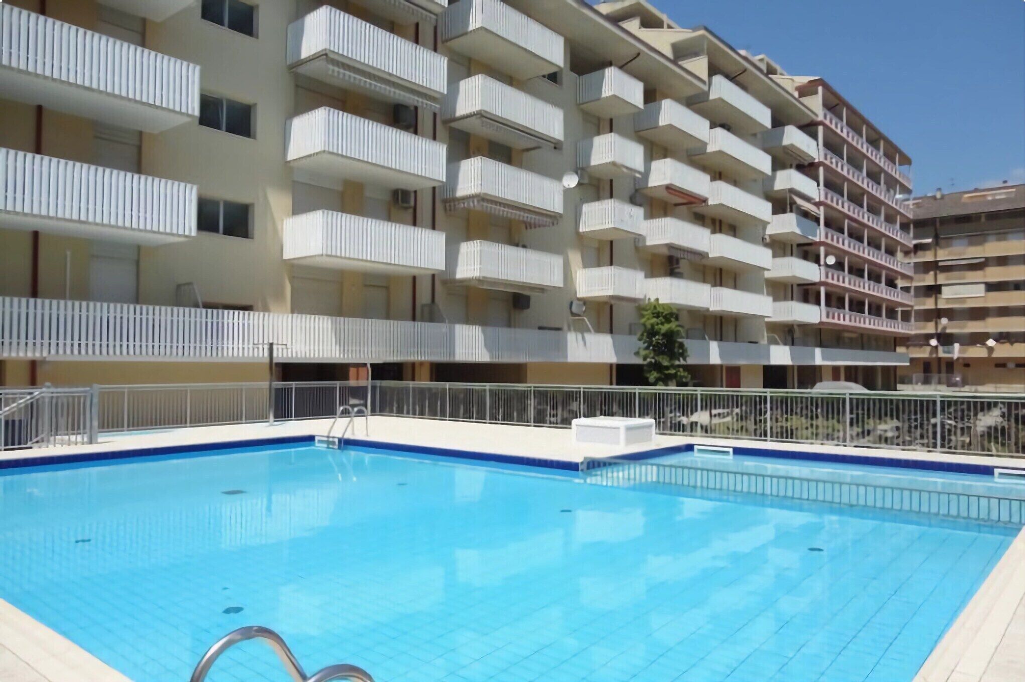 A swimming pool with a metal ladder, surrounded by a white fence.