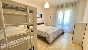 Une chambre avec des lits superposés, un lit simple, une table de chevet avec une lampe, une armoire et une fenêtre avec des rideaux.