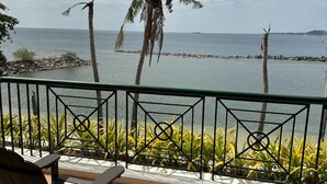 Un balcon avec des sièges d’extérieur, une vue sur la mer et des palmiers.