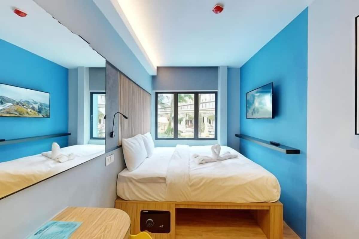 A modern hotel room with a bed, bedside tables, a TV, and a window.