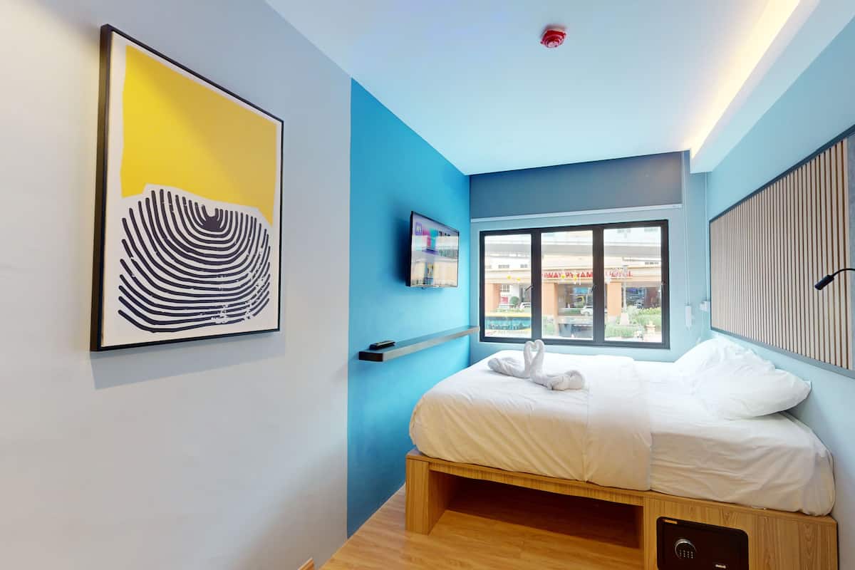 A modern hotel room with a bed, a window with a view of the outside, a mounted TV, and a wall-mounted artwork.
