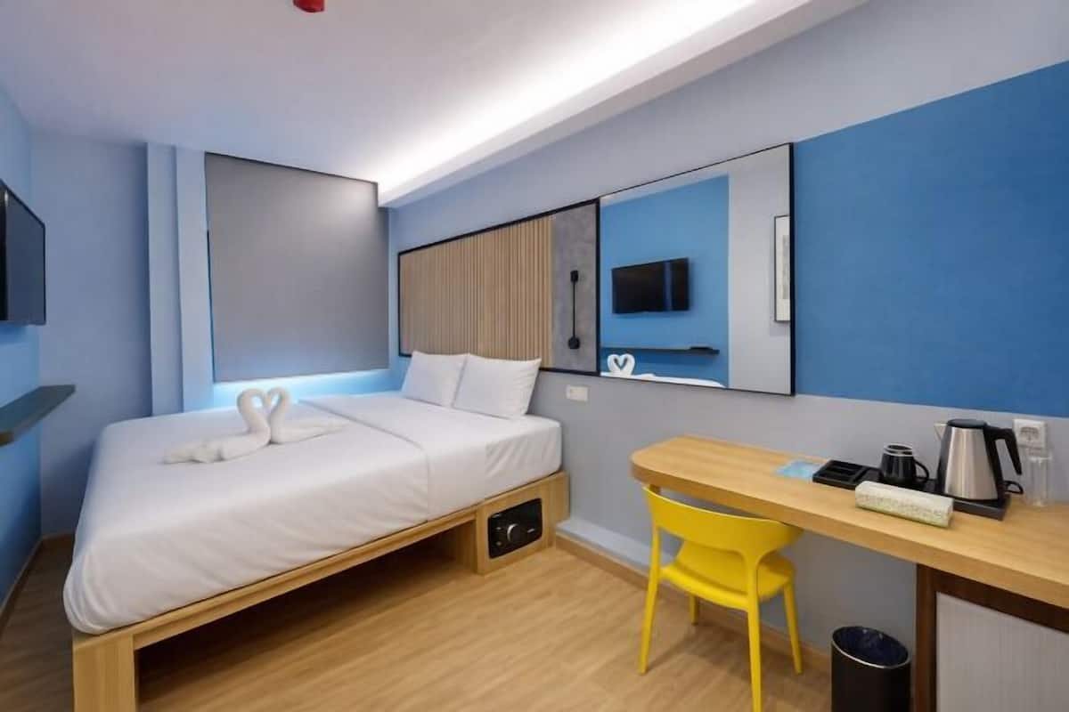 A compact hotel room with a single bed, a desk, a chair, a TV, and a coffee maker.