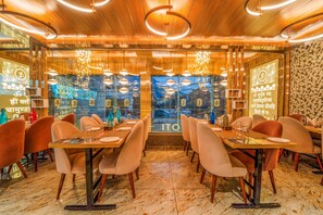 A restaurant with wooden ceiling, hanging lights, and a view through large windows. Tables are set with plates and glasses. - Hotel The Grand Dewan (Reasi)