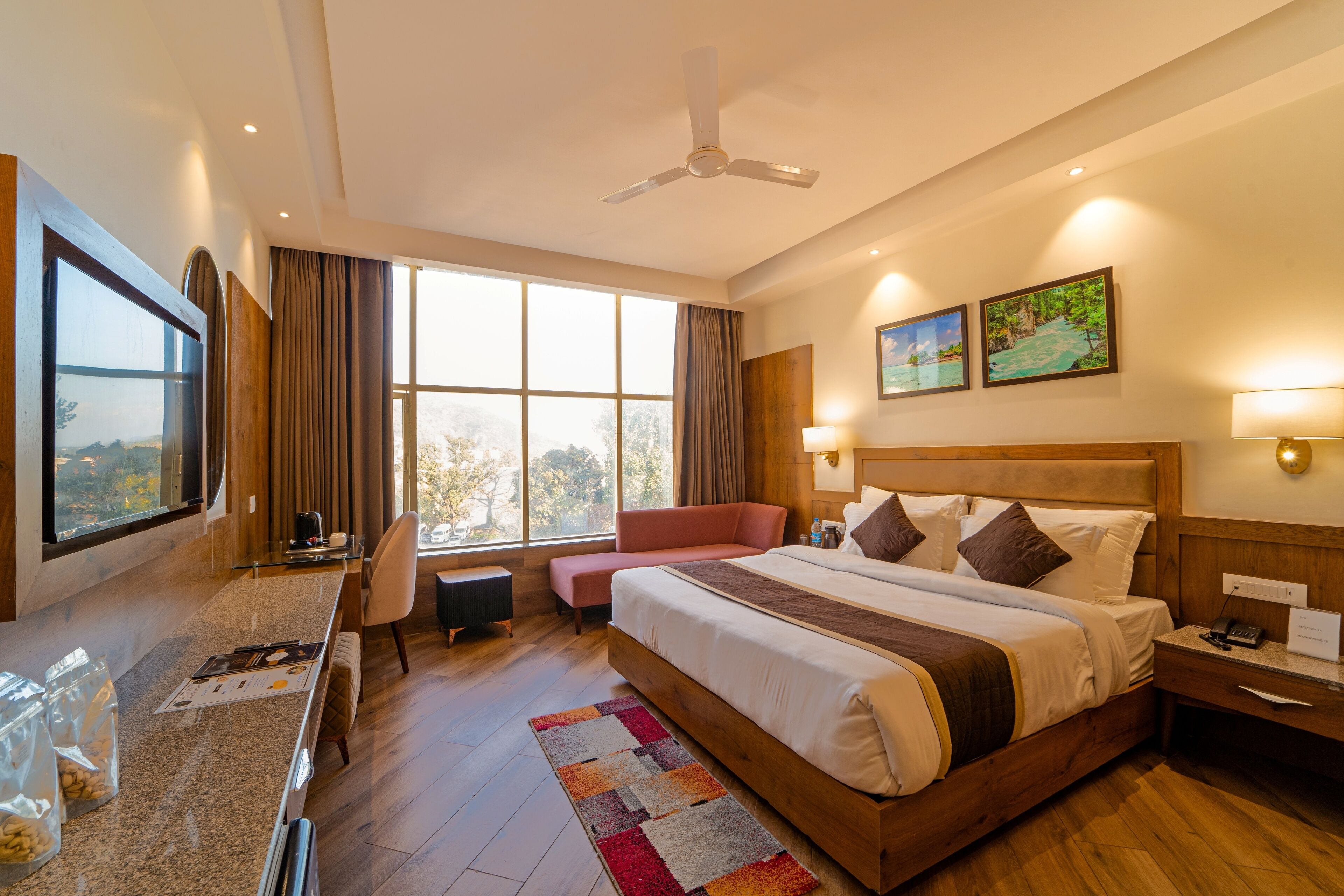A hotel room with a large bed, a desk with a chair, a window with curtains, and a ceiling fan.