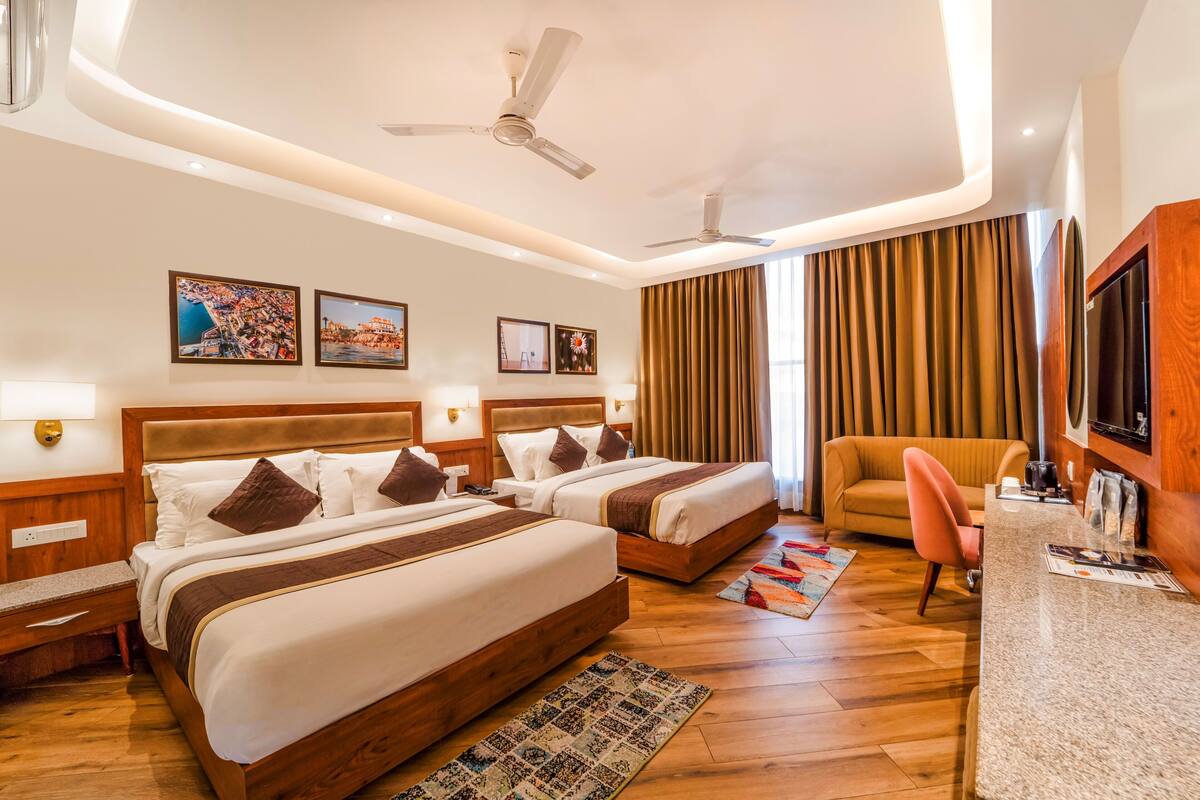A hotel room with two beds, a desk, a chair, and a TV.