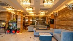 Um hall com piso de mármore, área de estar com sofás e mesa de centro, plantas em vasos e um grande lustre.