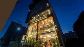 Um hotel moderno com fachada de vidro, sinalização iluminada e um restaurante visível chamado "NAV JYOTE RESTAURANT".