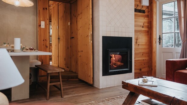 Een gezellig interieur van een chalet met een open haard, houten wanden, een eethoek en een raam met gordijnen.