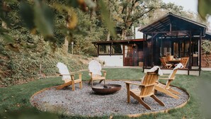 Een rond zitgedeelte met Adirondack-stoelen en een vuurkuil, omgeven door een grindpad, met een gebouw op de achtergrond.