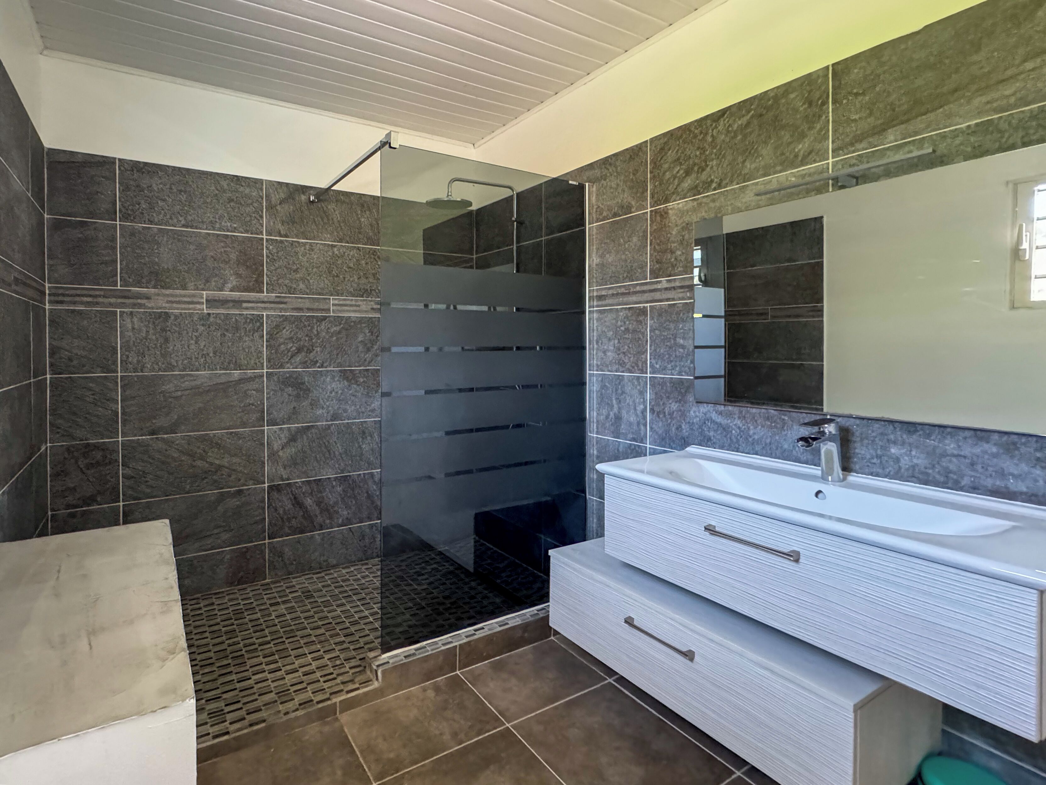 A modern bathroom with a glass shower enclosure, a large mirror, and a white vanity with drawers.
