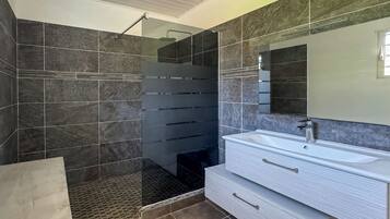 A modern bathroom with a glass shower enclosure, a large mirror, and a white vanity with drawers.