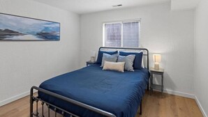 Ein Schlafzimmer mit Bett, Nachttischen, einem Fenster mit Jalousien und einer Deckenleuchte.